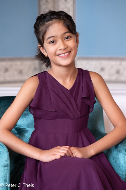 Joy Pullagurla seated in a plum recital dress